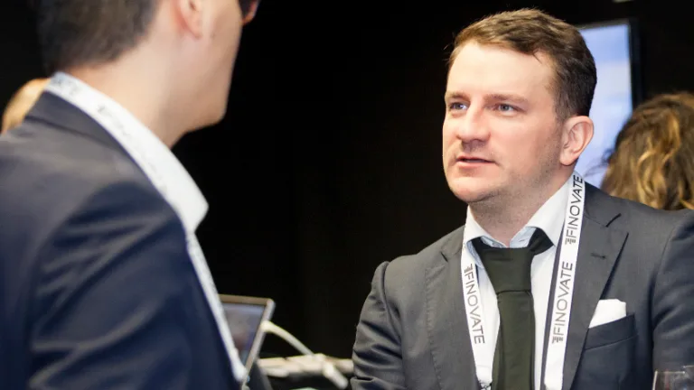 Man wearing a Finovate conference lanyard talking with a colleague